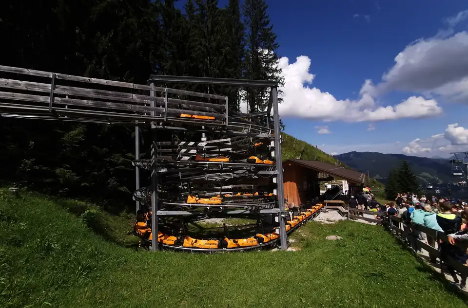 Orange Coaster-Schlitten warten übereinander in einer spiralförmigen Abstellanlage aus Holz und Stahl